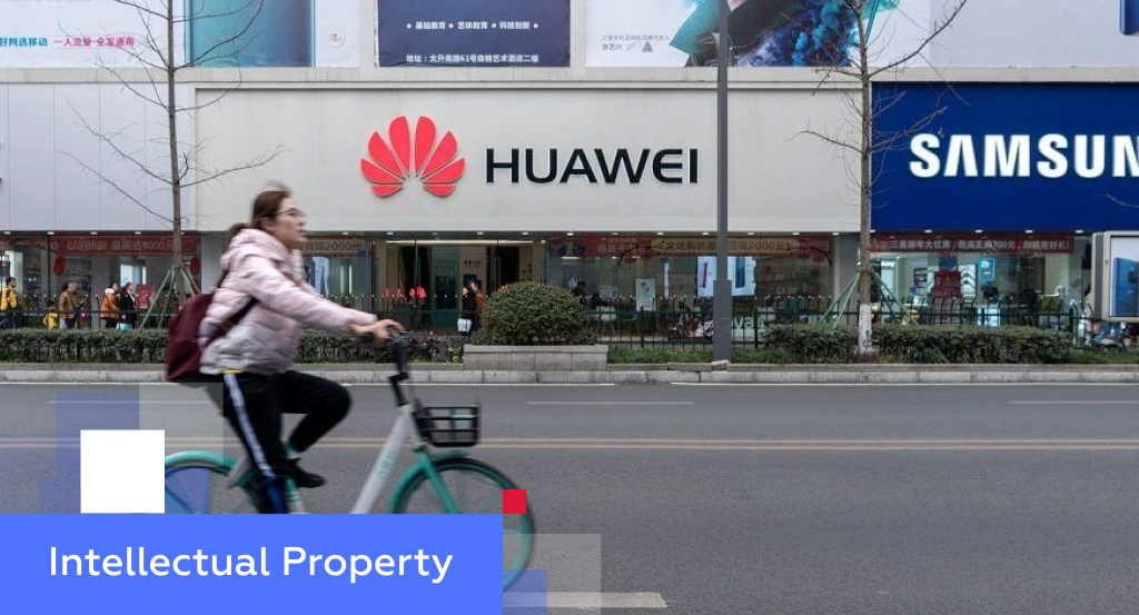Cyclist passing Huawei and Samsung electronics storefronts side by side on a Chinese street — illustrating intellectual property protection in China